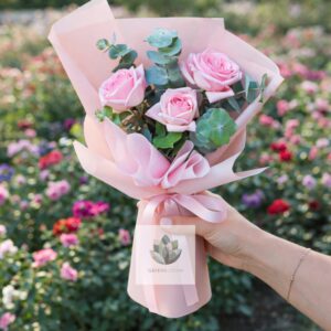 pink rose bouquet with eucalyptus wrapped in pink paper held in hand in a flower garden – fresh flower delivery Lebanon Greenbloom florist